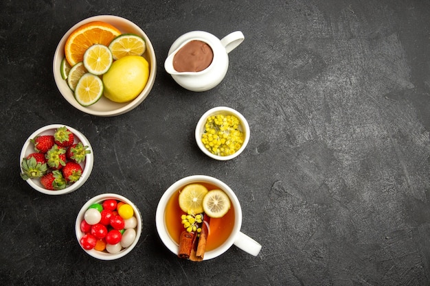 Top view from afar sweets on the table bowls of strawberries and herbs and a cup of tea with lemon and cinnamon sticks