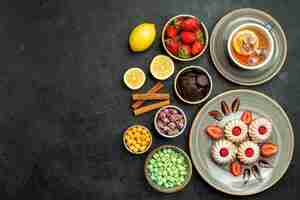 Free photo top view from afar sweets with tea cookies with strawberry black tea with lemon hizelnuts bowls of chocolate and different sweets on the right side of table