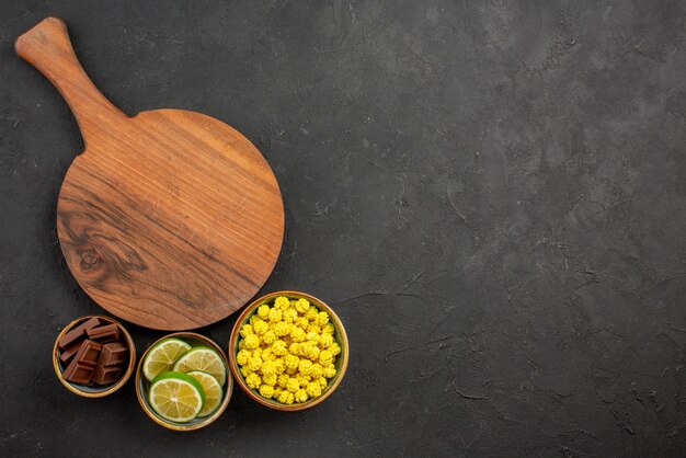 Top view from afar sweets wooden cutting board next to the bowls of chocolate limes and yellow candies on the left side of the table