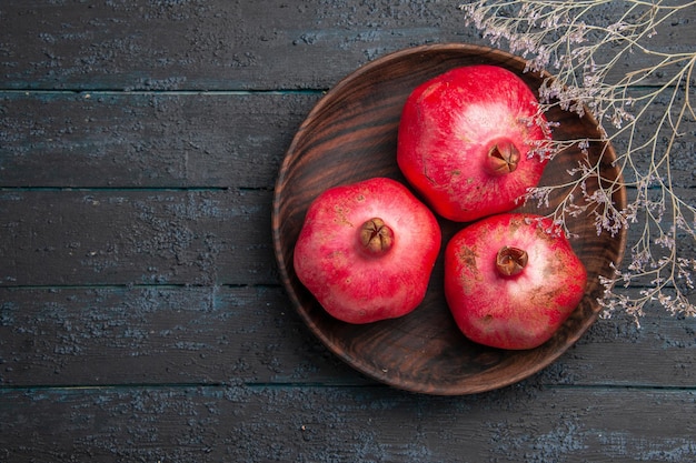 Top view from afar three pomegranates wooden bowl of pomegranates next to the branches on grey table