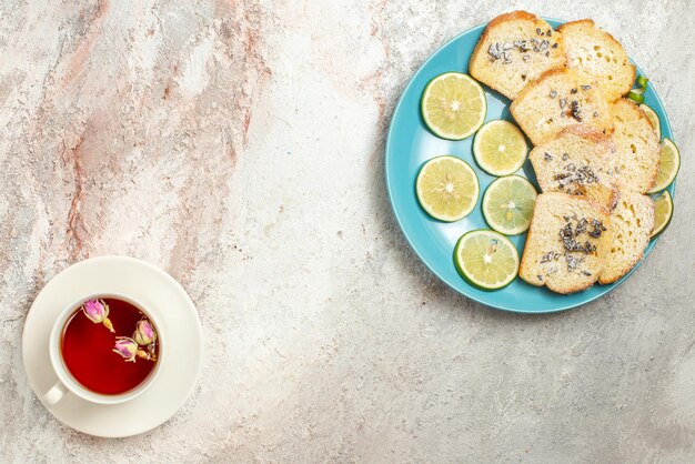 ケーキの青いプレートの横にある受け皿にお茶の白いカップと紅茶のカップとテーブルのスライスされたライムと離れた皿からの上面図