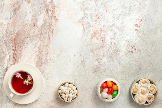 Vista dall'alto da lontano i dolci con una tazza di ciotole da tè di diversi dolci e una tazza di tè nero sul tavolo