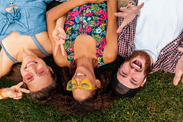 Top view from above on colorful stylish happy young company of friends lying on grass in park, man and women having fun together