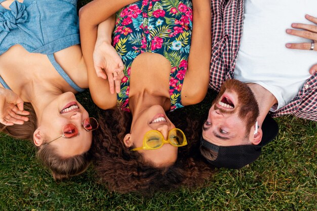 Top view from above on colorful stylish happy young company of friends lying on grass in park, man and women having fun together