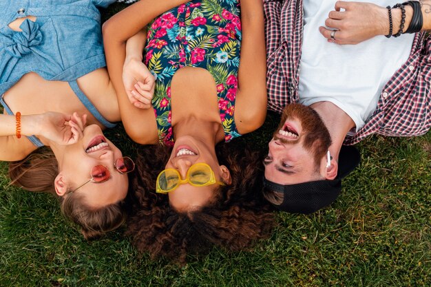 Top view from above on colorful stylish happy young company of friends lying on grass in park, man and women having fun together