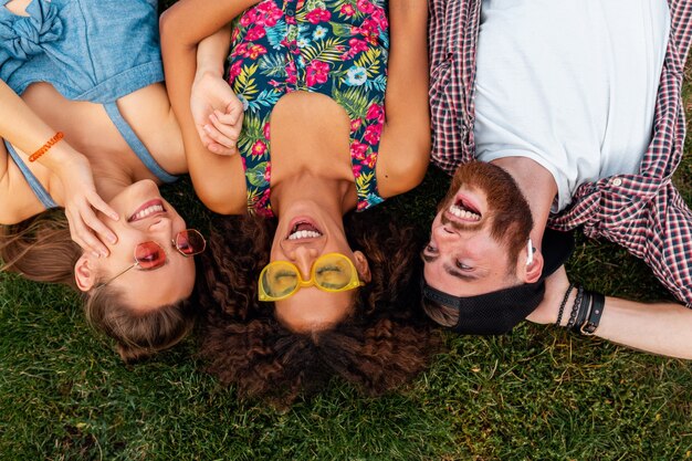 Top view from above on colorful stylish happy young company of friends lying on grass in park, man and women having fun together