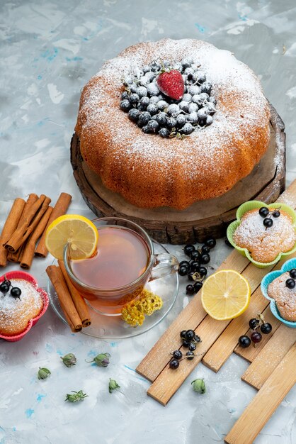 A top view fruit cake delicious and round formed with fresh blue, berries and along with cup of tea on bright cake