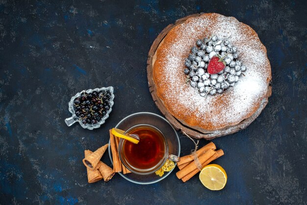 A top view fruit cake delicious and round formed with fresh blue, berries and along with cup of tea on cake biscuit sweet sugar
