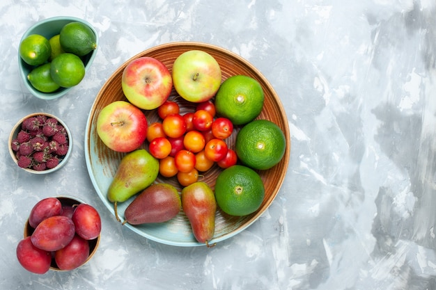 Top view fruit composition apples pears tangerines and plums on the light white desk.