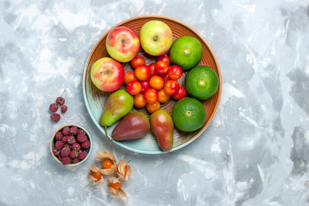 Top view fruit composition apples pears tangerines and plums on the white desk.