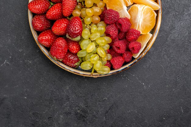 Top view fruit composition strawberries grapes raspberries and tangerines inside tray on a dark space