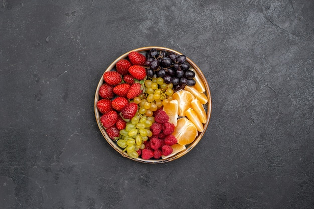 Top view fruit composition strawberries grapes raspberries and tangerines inside tray on dark space