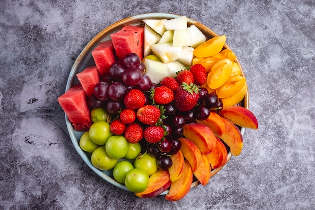 Top view of fruit plate with watermelon greengage plum grape peach apricot strawberry melon and cherry