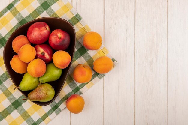 Top view of fruits as apricot peach pear in bowl on plaid cloth and on wooden background with copy space