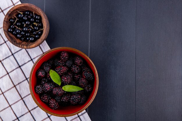 Top view of fruits as bowls of sloe and blackberry on plaid cloth on black surface