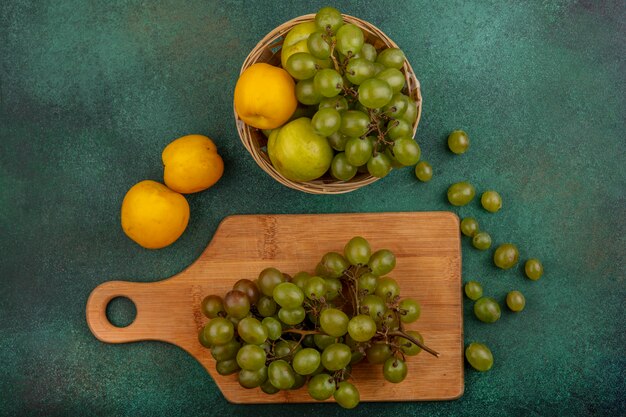 Top view of fruits as bunch of grape on cutting board and nectacot pluot and grape in basket with grape berries on green background