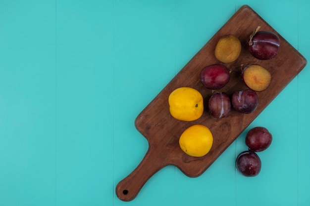 Vista dall'alto di frutti tagliati e interi pluots e nettacots sul tagliere e su sfondo blu con copia spazio