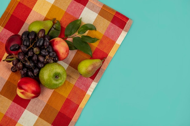 格子縞の布とコピースペースと青い背景に葉を持つブドウ桃リンゴ梨としての果物の上面図