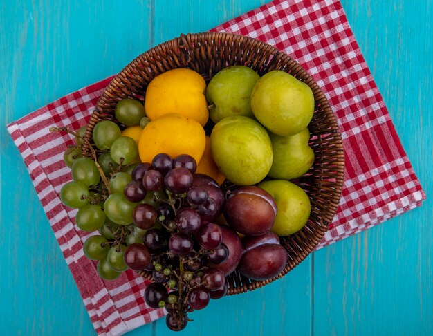 ブドウが格子縞の布と青い背景の上のバスケットにネクタコットをプルオットとして果物の上面図