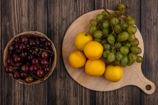 Free photo top view of fruits as nectacots and white grape on cutting board with basket of black grape on wooden background