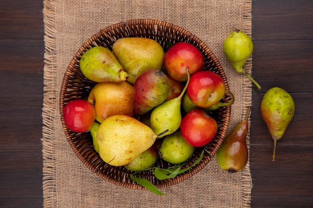Top view of fruits as peach apple plum in basket and on sackcloth on wooden surface