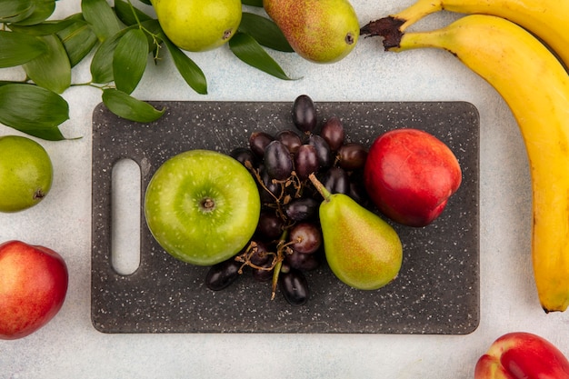 Top view of fruits as pear apple grape peach on cutting board with banana and leaves on white background