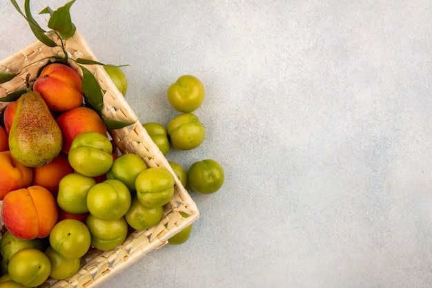 Top view of fruits as pear apricot plum in basket and on white background with copy space