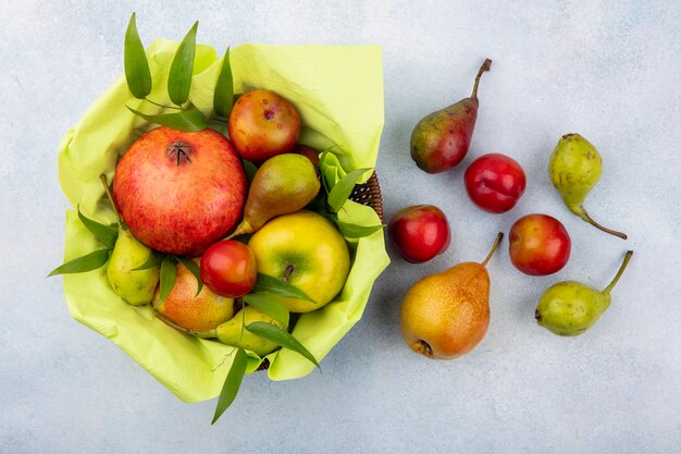 Top view of fruits as plum apple peach and pomegranate in basket and on white surface