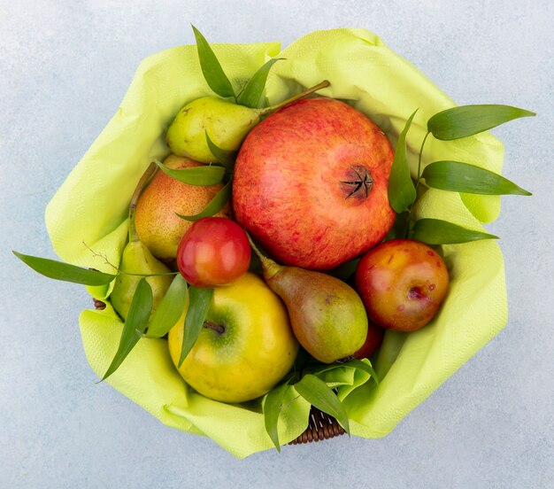 Top view of fruits as plum apple peach and pomegranate in basket on white surface