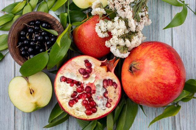 Top view of fruits as pomegranate and apple halves with whole ones and bowl of blackthorn with flowers and leaves on black surface