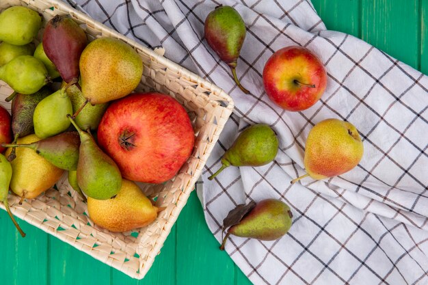 チェック柄の布と緑の表面のバスケットにザクロと桃として果物のトップビュー