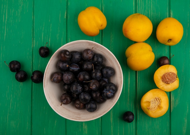 Top view of fruits as sloe berries in bowl and apricots with half cut one on green background