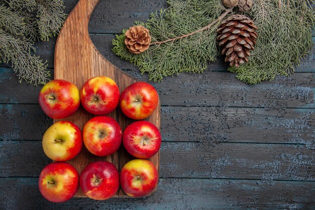 Top view fruits on board yellow-reddish apples on a cutting board on grey surface and tree branches with cones