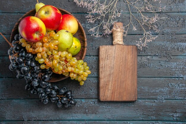 흰색과 검은색 포도 라임 사과 배의 그릇에 있는 상위 뷰 과일과 회색 표면에 있는 나뭇가지 옆