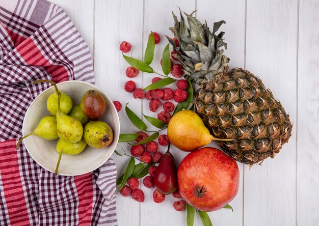 Top view of fruits and bowl of pears on plaid cloth with leaves on wooden surface