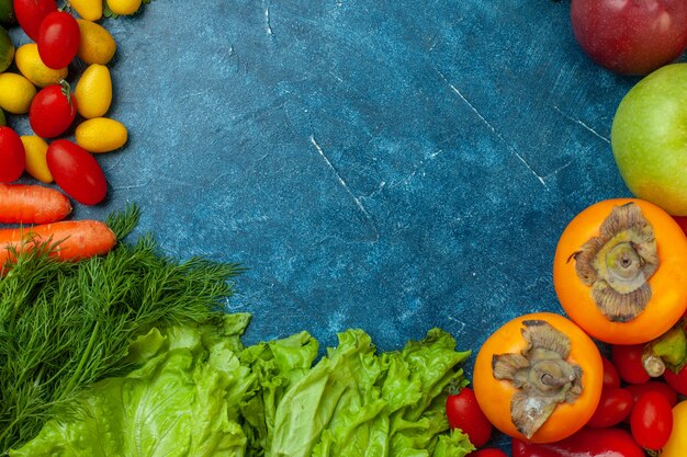 Top view fruits and vegetables parsley lettuce cherry tomatoes cumcuat persimmon apples on blue background