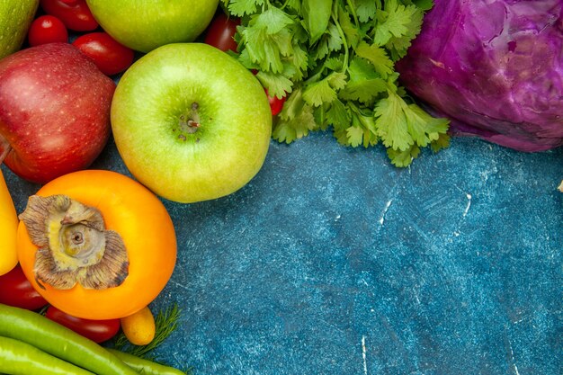 Top view fruits and vegetables red cabbage cherry tomato coriander apples persimmons on blue table