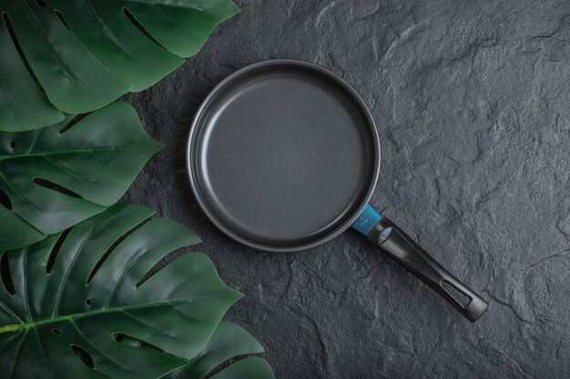 Top view of frying pan over black background with green leaves.