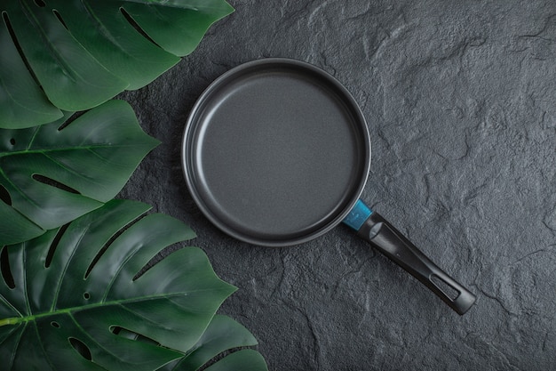 Top view of frying pan over black background with green leaves.