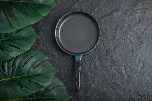 Top view of frying pan over black background with green leaves.