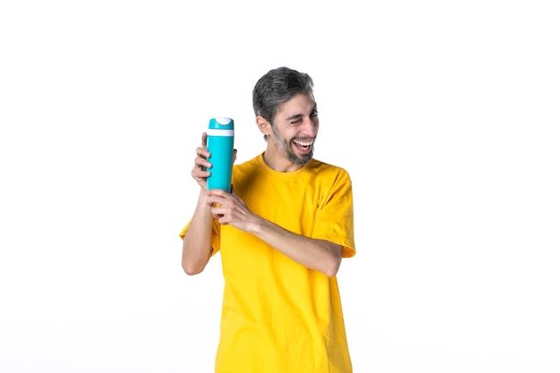 白い背景の上の魔法瓶を保持している黄色のシャツの面白い若い男性の上面図