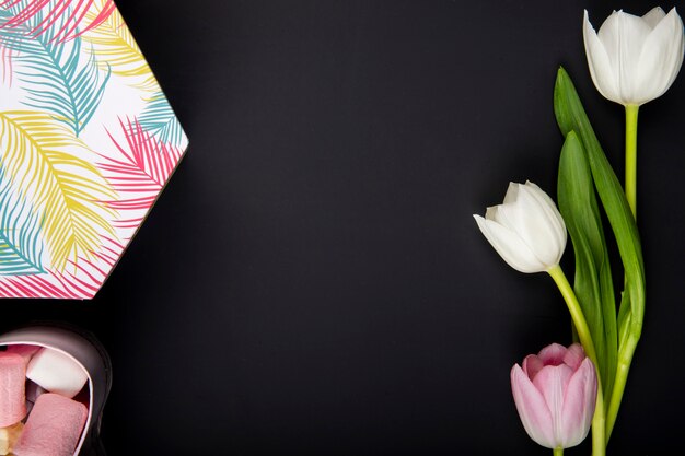 Вид сверху подарочной коробке с зефиром и тюльпанами белого и розового цвета на черном столе с копией пространства