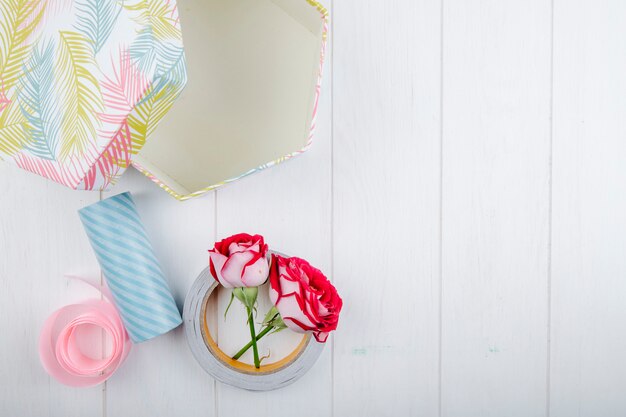 Free photo top view of gift box and red color roses with rolls of adhesive tape on white wooden background with copy space