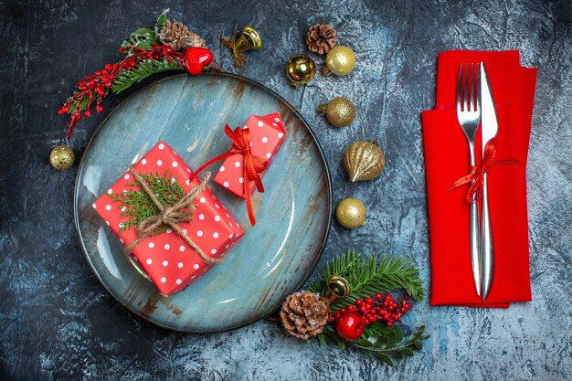 Top view of gift boxes on a blue plate decorative accessories conifer cone and cutlery set with red ribbon on dark background