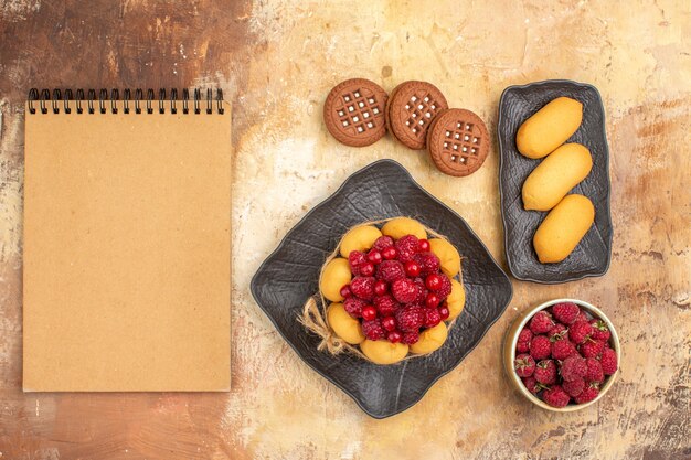 Вид сверху подарочного торта и печенья на коричневых тарелках, фруктов и ноутбука на столе смешанных цветов
