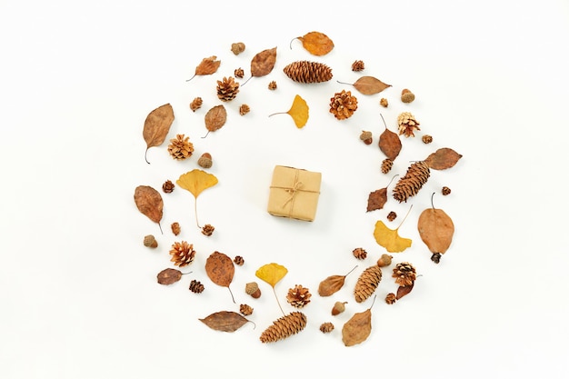 Top view of a gift in the middle of a wreath made of autumn leaves and conifer cones on white backgr
