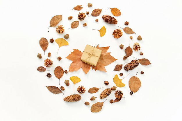 Top view of a gift in the middle of a wreath made of autumn leaves and conifer cones on white