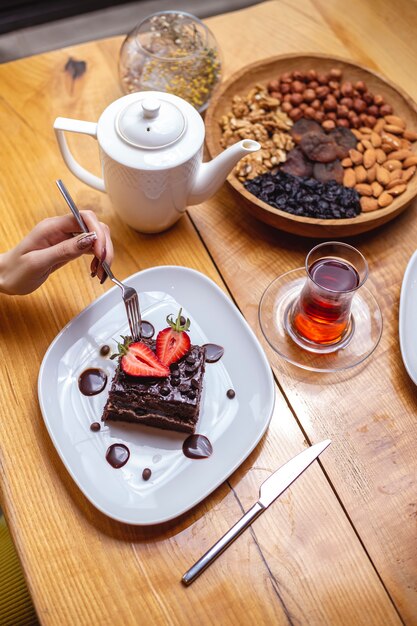 Вид сверху девушка ест шоколадный торт с чашкой чая и орехами
