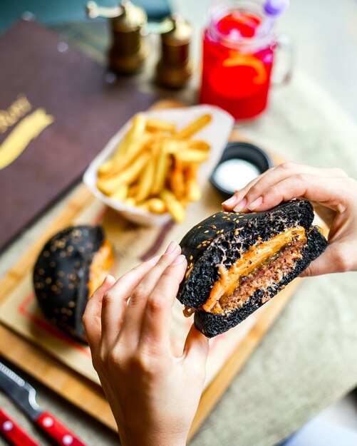 トップビューの女の子は、フライドポテトと黒パンで肉バーガーを食べる