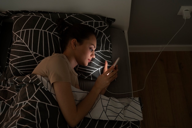 Вид сверху девушка лежит в постели со смартфоном